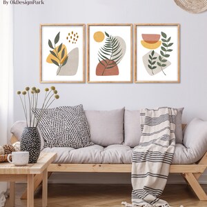 Puede incluir: Tres impresiones de arte abstracto enmarcadas con un dise&ntilde;o minimalista que presenta hojas verdes, formas amarillas y naranjas y un fondo blanco.