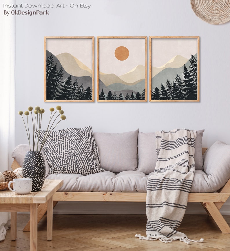 K&ouml;nnte beinhalten: Drei gerahmte Drucke einer minimalistischen Landschaft mit Bergen, B&auml;umen und einer Sonne. Die Drucke sind in einem hellbraunen Rahmen und h&auml;ngen an einer wei&szlig;en Wand &uuml;ber einem hellgrauen Sofa.