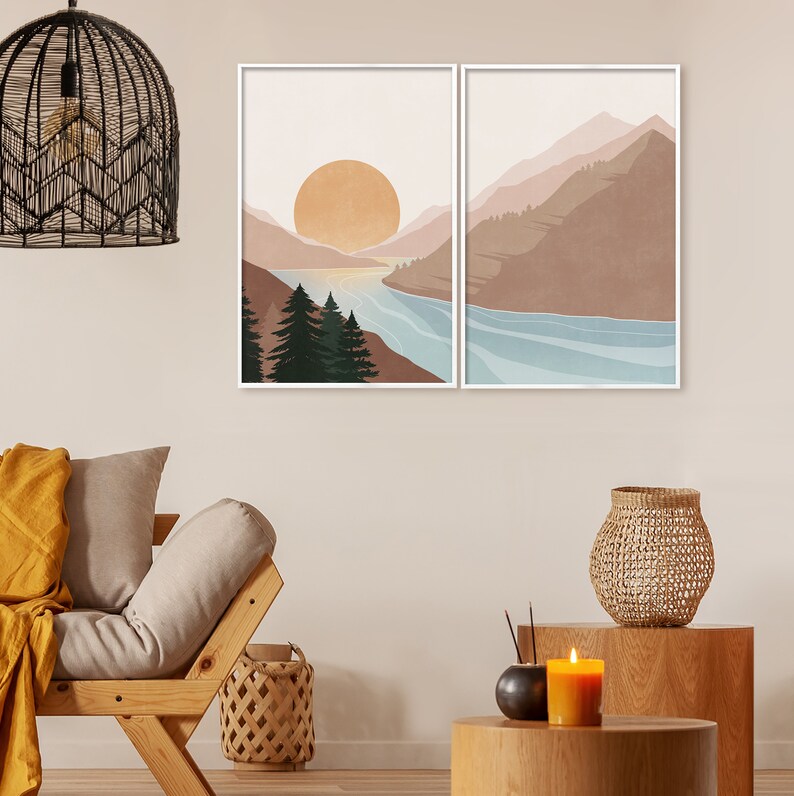 K&ouml;nnte beinhalten: Zwei minimalistische Landschaftsdrucke mit einer Bergkette, einem Fluss und einer gro&szlig;en Sonne im Hintergrund. Die Drucke sind in Wei&szlig; gerahmt und an einer hellbeigen Wand aufgeh&auml;ngt.