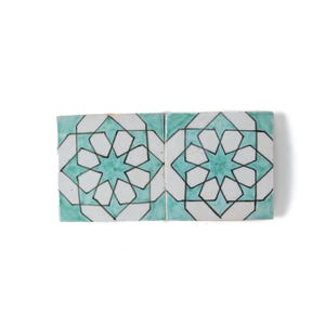 Könnte beinhalten: Vier quadratische Keramikfliesen mit einem geometrischen Sternmuster. Das Design zeigt einen türkisfarbenen Stern in der Mitte, umgeben von Weiß und schwarz umrandet. Die Fliesen sind quadratisch angeordnet.