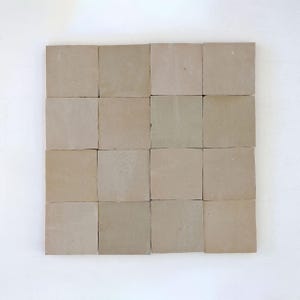 May include: Sixteen square, beige tiles arranged in a grid. The tiles have a matte finish and a slightly uneven surface, suggesting a natural material. The neutral colour palette makes them suitable for various design applications. Each tile is approximately 15 cm x 15 cm.