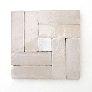 Puede incluir: Disposición cuadrada de baldosas rectangulares blanquecinas. Las baldosas están dispuestas en espiga, con una sola baldosa cuadrada en el centro. Las baldosas tienen un acabado brillante y probablemente son de cerámica o porcelana.