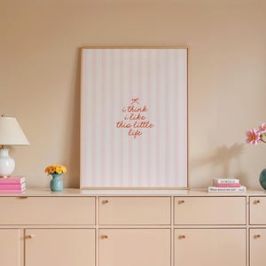 May include: A framed print with pink and white stripes and the text "i think i like this little life" in red.