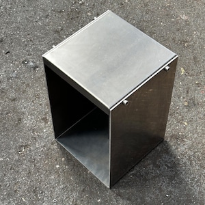 May include: A silver metal stool with a square top and open sides. The stool is made of metal and has a smooth, polished finish.