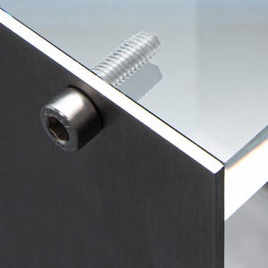 May include: Close-up of a silver metal screw and nut attaching a piece of glass to a metal surface.
