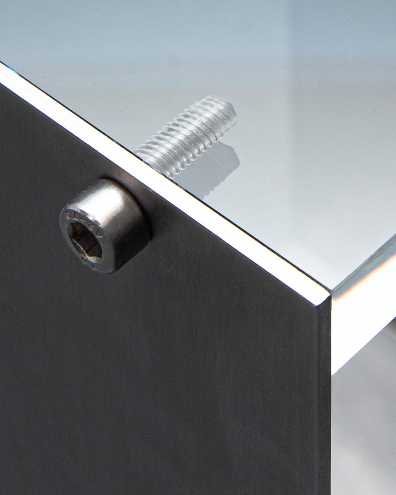 May include: Close-up of a silver metal screw and nut attaching a piece of glass to a metal surface.
