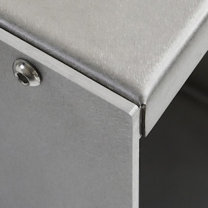 May include: Close-up of a silver metal box with a seam along the top edge. A single screw is visible on the side of the box.