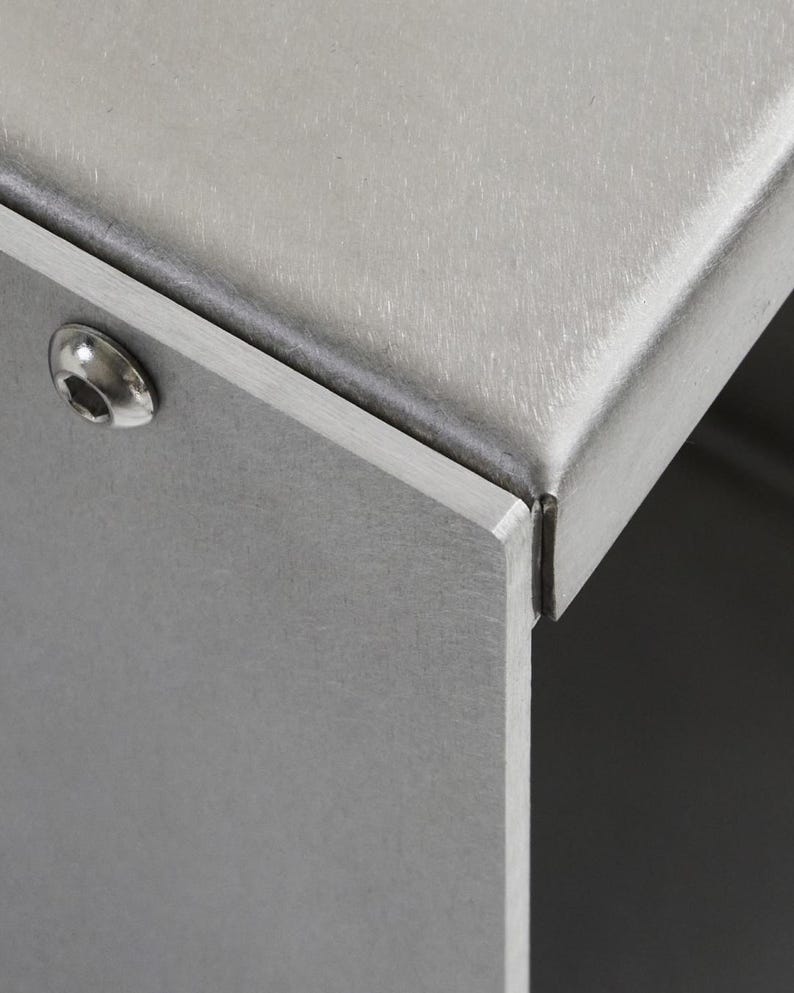 May include: Close-up of a silver metal box with a seam along the top edge. A single screw is visible on the side of the box.