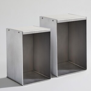 May include: Two silver metal cube shelves, one slightly larger than the other, are stacked on top of each other. The shelves are open on all sides and have a smooth, brushed finish.