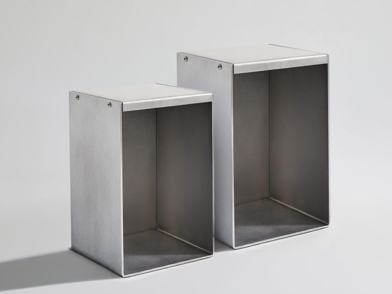May include: Two silver metal cube shelves, one slightly larger than the other, are stacked on top of each other. The shelves are open on all sides and have a smooth, brushed finish.
