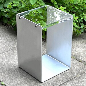 May include: A silver metal side table with a clear glass top. The table has a square base and a simple, modern design.