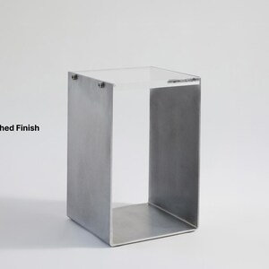 May include: A brushed metal side table with a square top and open sides. The table is made of metal and has a brushed finish.