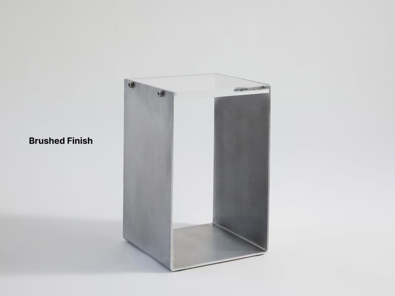 May include: A brushed metal side table with a square top and open sides. The table is made of metal and has a brushed finish.