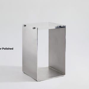 May include: A silver metal stand with a square top and open sides. The stand is made of polished metal and has a reflective surface.  "Mirror Polished" is written in black text below the stand.