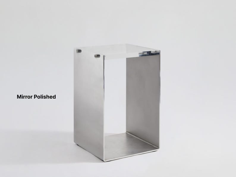 May include: A silver metal stand with a square top and open sides. The stand is made of polished metal and has a reflective surface.  "Mirror Polished" is written in black text below the stand.