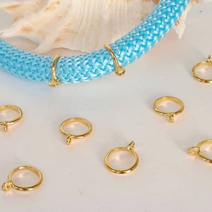 May include: Eight gold-colored metal rings with a small loop on one side. The rings are scattered on a white surface.