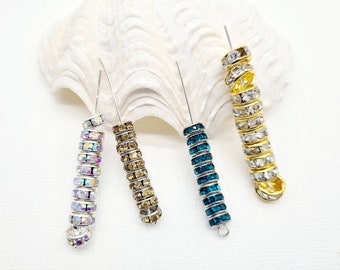 May include: Four strands of rhinestone beading in different colors. The strands are coiled and have a silver wire running through them. The colors are iridescent, gold, teal, and clear.
