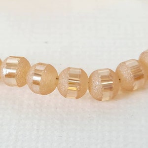 Peut inclure: Un brin de perles de verre de couleur pêche avec une finition givrée et des accents dorés. Les perles sont rondes et ont un design facetté.