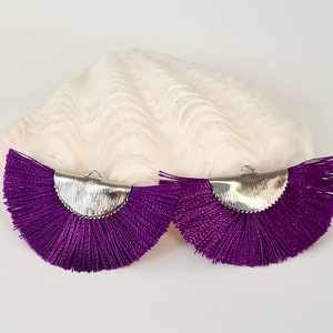 Peut inclure: Une paire de boucles d'oreilles en forme de pompon violet avec des accents en métal argenté. Les pompons sont en forme d'éventail et ont une texture de frange.