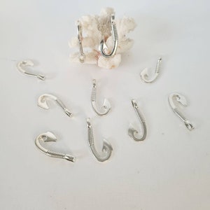 Könnte beinhalten: Eine Gruppe von silberfarbenen Angelhaken-Anhängern, verstreut auf einer weißen Oberfläche. Die Haken sind mit einem strukturierten Design verziert und haben eine Öse oben zum Anbringen an Schmuck oder anderen Bastelarbeiten.