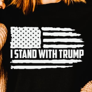 May include: Black t-shirt with a distressed white graphic of the American flag and the text "I Stand With Trump." The shirt is a PNG sublimation file.
