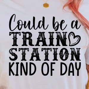 May include: White t-shirt with black text that reads "Could be a TRAIN STATION KIND OF DAY". The text has a distressed look. A small red heart is next to the word "TRAIN".