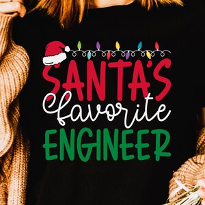 May include: Black t-shirt with the text "SANTA'S favorite ENGINEER" in red, white, and green. The design includes a Santa hat and string lights. The words "DIGITAL PRODUCT | SVG | PNG | EPS | PDF | DXF INSTANT DOWNLOAD" are at the bottom.