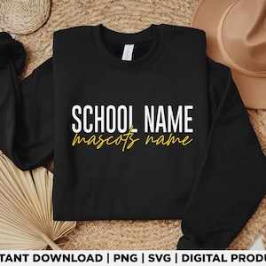 May include: A black crewneck sweatshirt with the text "SCHOOL NAME" in white block letters and "mascots name" in yellow script. The sweatshirt is displayed on a woven surface with a straw hat in the background.