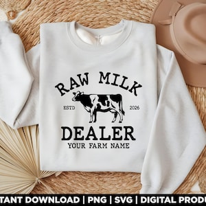 Può includere: Una felpa girocollo grigio chiaro con una grafica nera di una mucca. Il testo recita RAW MILK DEALER, ESTD 2026 e YOUR FARM NAME. Il design è centrato sul petto, mostrando un carattere in grassetto e un'illustrazione dettagliata di una mucca.