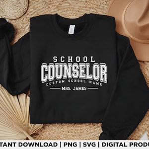 Może przedstawiać: Czarna bluza z białym napisem "SCHOOL COUNSELOR" w dużych literach. Poniżej znajduje się napis "CUSTOM SCHOOL NAME" i "MRS. JAMES". Jest to produkt cyfrowy.