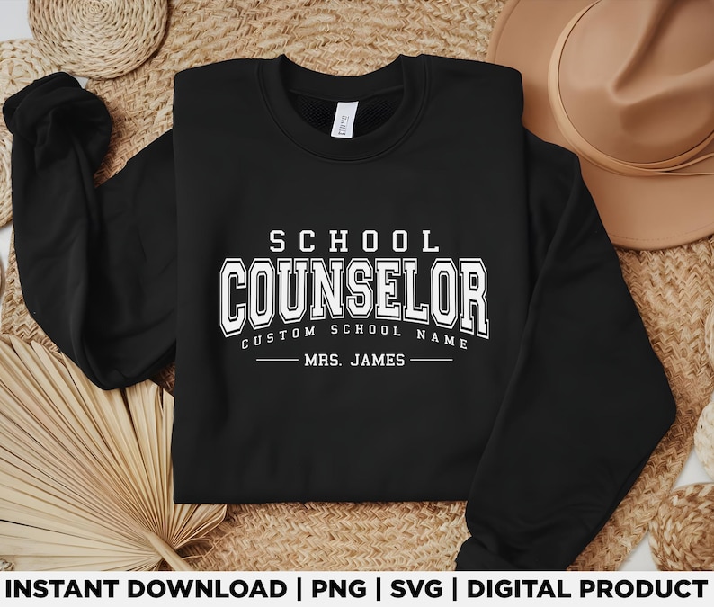 Może przedstawiać: Czarna bluza z białym napisem "SCHOOL COUNSELOR" w dużych literach. Poniżej znajduje się napis "CUSTOM SCHOOL NAME" i "MRS. JAMES". Jest to produkt cyfrowy.