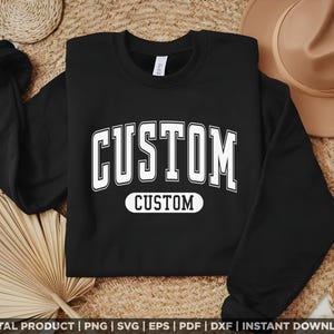 May include: Black crew neck sweatshirt featuring the word "CUSTOM" in large white block letters. The word "CUSTOM" is also displayed in a white oval below. The sweatshirt is on a woven surface.
