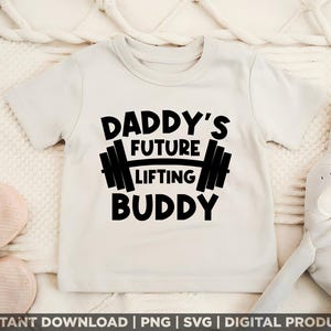 Peut inclure: Un t-shirt de bébé beige clair avec le texte "DADDY'S FUTURE LIFTING BUDDY" en lettres noires grasses. Le design comprend un haltère. Le t-shirt est à manches courtes et a un col rond.