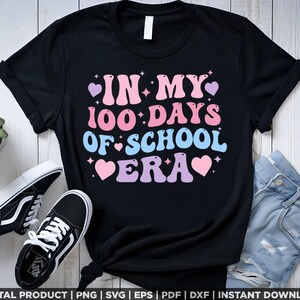 May include: Black t-shirt with a pink, blue, and white graphic that says "In My 100 Days Of School Era" with hearts and stars.