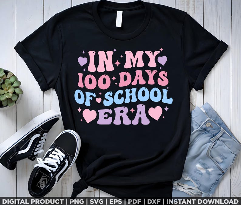 May include: Black t-shirt with a pink, blue, and white graphic that says "In My 100 Days Of School Era" with hearts and stars.