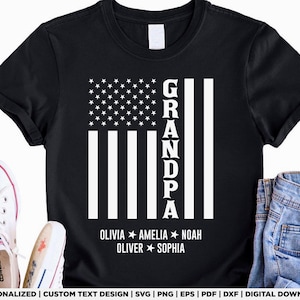 May include: Black t-shirt with a white American flag design and the word "GRANDPA" in vertical text. Underneath the flag are the names OLIVIA, AMELIA, NOAH, OLIVER, and SOPHIA. The shirt is shown with white trainers and blue jeans.