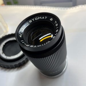 May include: A black camera lens with the text "INTENS-4/135 ABTOMAT 781673" printed on the side.