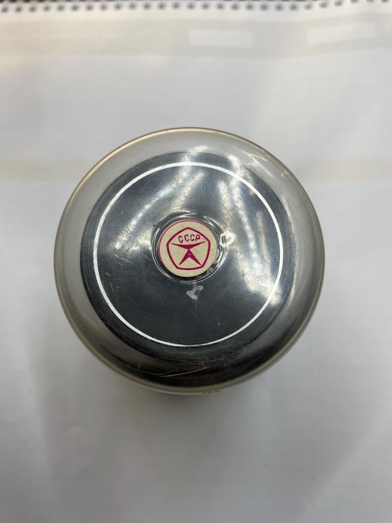 May include: A silver metal container with a black lid and a red and white sticker that says "CCCP" in Cyrillic lettering.