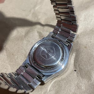 以下が含まれることがあります： 金属製のリンクバンドが付いたシルバーカラーの腕時計。円形のケースバックはステンレススチール製で、中央にキリル文字で「CCCP」と刻印された星のエンブレムがデザインされており、その起源と製造元を示しています。