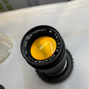 May include: A black camera lens with the text "KONTEPER-II 4/135 ABTOMAT 6" and a yellow filter.