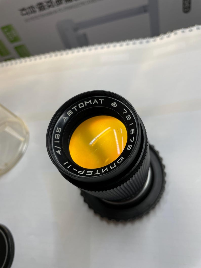 May include: A black camera lens with the text "KONTEPER-II 4/135 ABTOMAT 6" and a yellow filter.