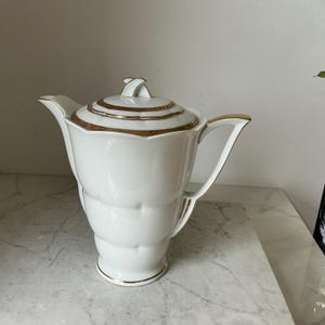 Puede incluir: Tetera de porcelana blanca con ribetes dorados. La tetera tiene un diseño único y acanalado y una tapa con un asa decorativa. El asa y el pico también están adornados con oro. Una pieza clásica para servir té.