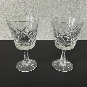 Op de afbeelding: Twee heldere kristallen wijnglazen met ingewikkelde diamant- en sterpatronen. De glazen hebben een voet en een brede kom. De glazen zijn gemaakt van helder glas en zijn perfect voor het serveren van wijn.