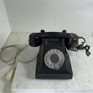 May include: A classic black rotary dial telephone with a clear dial and a black handset. The phone features a coiled cord and a plug. The phone is placed on a white marble surface.