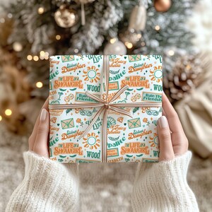 May include: A wrapped gift with a patterned paper featuring text and illustrations in teal, orange, and white. The gift is tied with a brown ribbon and bow. The text includes "The Life of a Showgirl" and "Eldest Daughter".