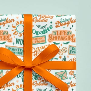 May include: Gift-wrapped present with white wrapping paper featuring teal and orange text and illustrations. The text includes phrases like "The Life of a Showgirl" and "The Fate of Ophelia." An orange ribbon is tied in a bow.