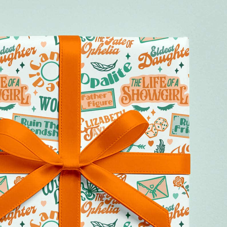 May include: Gift-wrapped present with white wrapping paper featuring teal and orange text and illustrations. The text includes phrases like "The Life of a Showgirl" and "The Fate of Ophelia." An orange ribbon is tied in a bow.