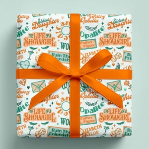 Showgirl inspired wrapping paper with graphics of TS12 tracks with a Christmas gift wrap orange bow.