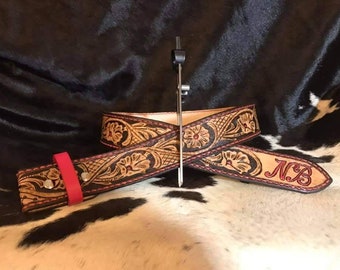 May include: A brown leather belt with intricate floral tooling and red stitching. The belt is personalized with the initials "N.B."