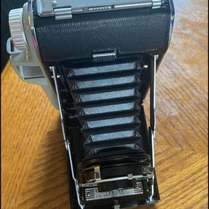 May include: A vintage black and silver folding camera with a bellows system and a lens with the text "KODAK" and "126" printed on it.